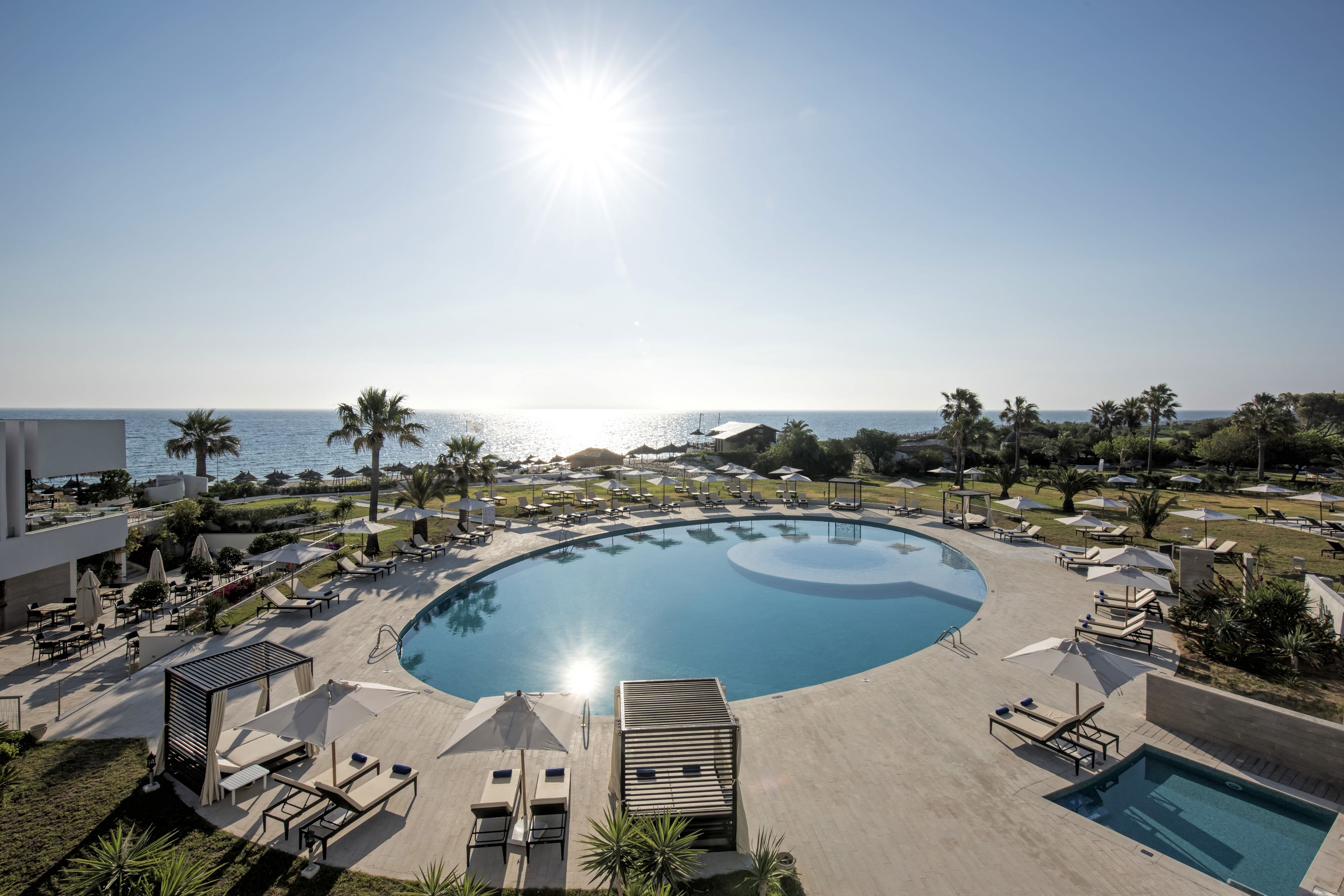 Ett poolområde på hotellet med solstolar, parasoller och utsikt över havet.