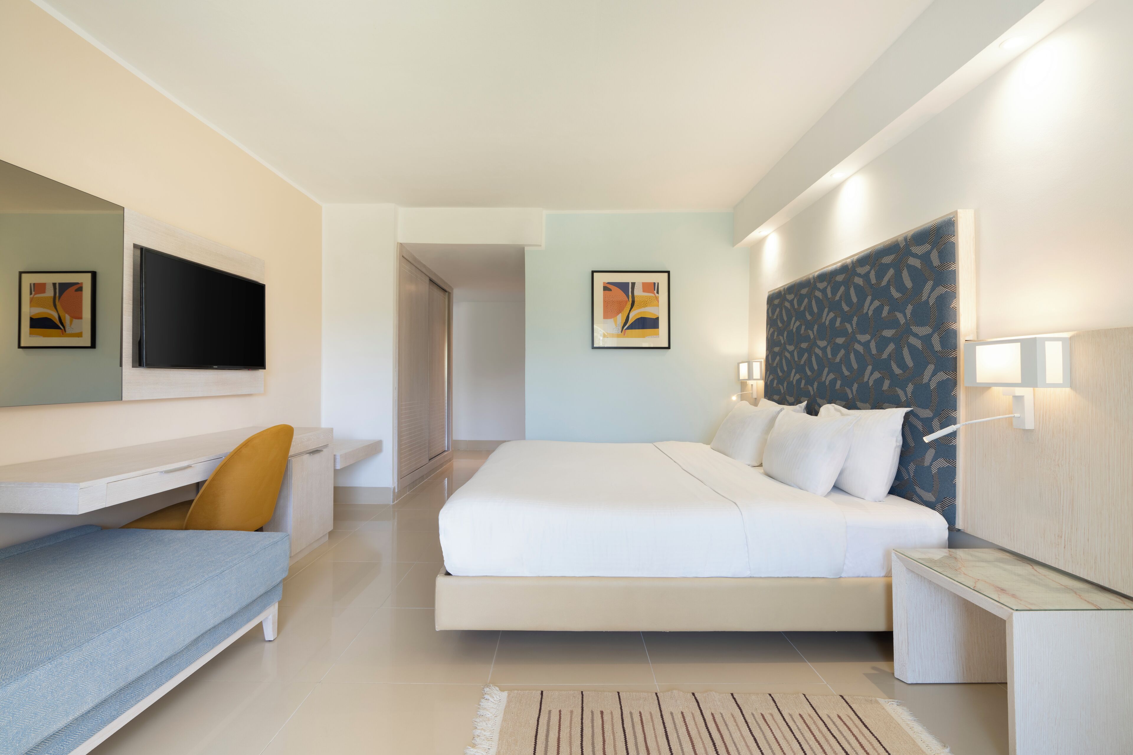 Een moderne hotelkamer met een groot bed, een bureau met stoel, een flatscreen televisie en een wandlamp.