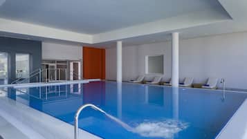 Una piscina interior con agua cristalina, un trampolín y sillones de descanso a un lado.