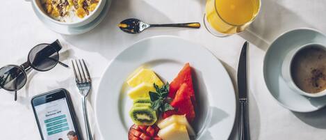 A breakfast setting with a plate of fruit, a bowl of cereal, a glass of orange juice, and a cup of coffee.