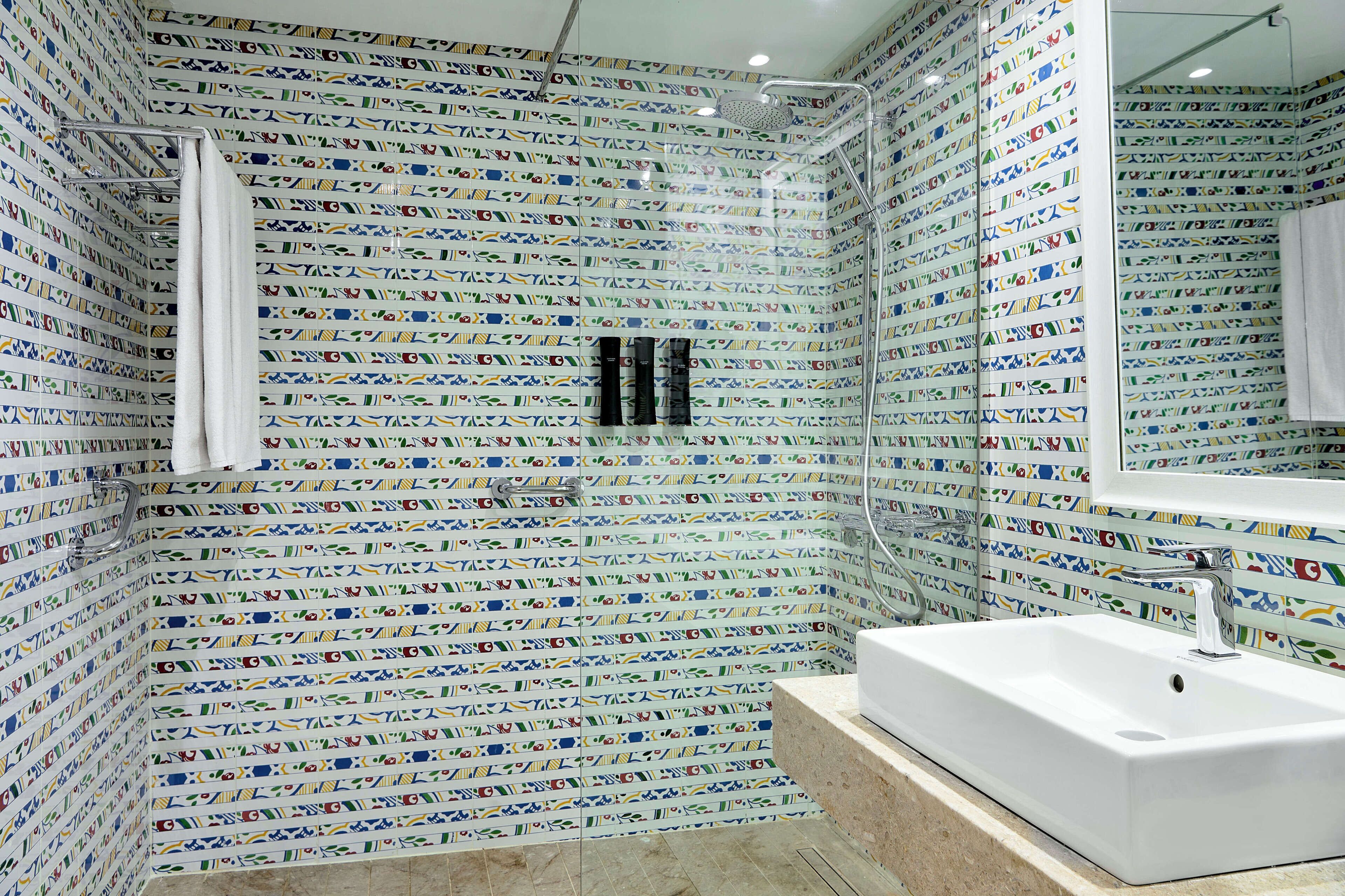 A bathroom with patterned tiles, a white sink, and a shower area.