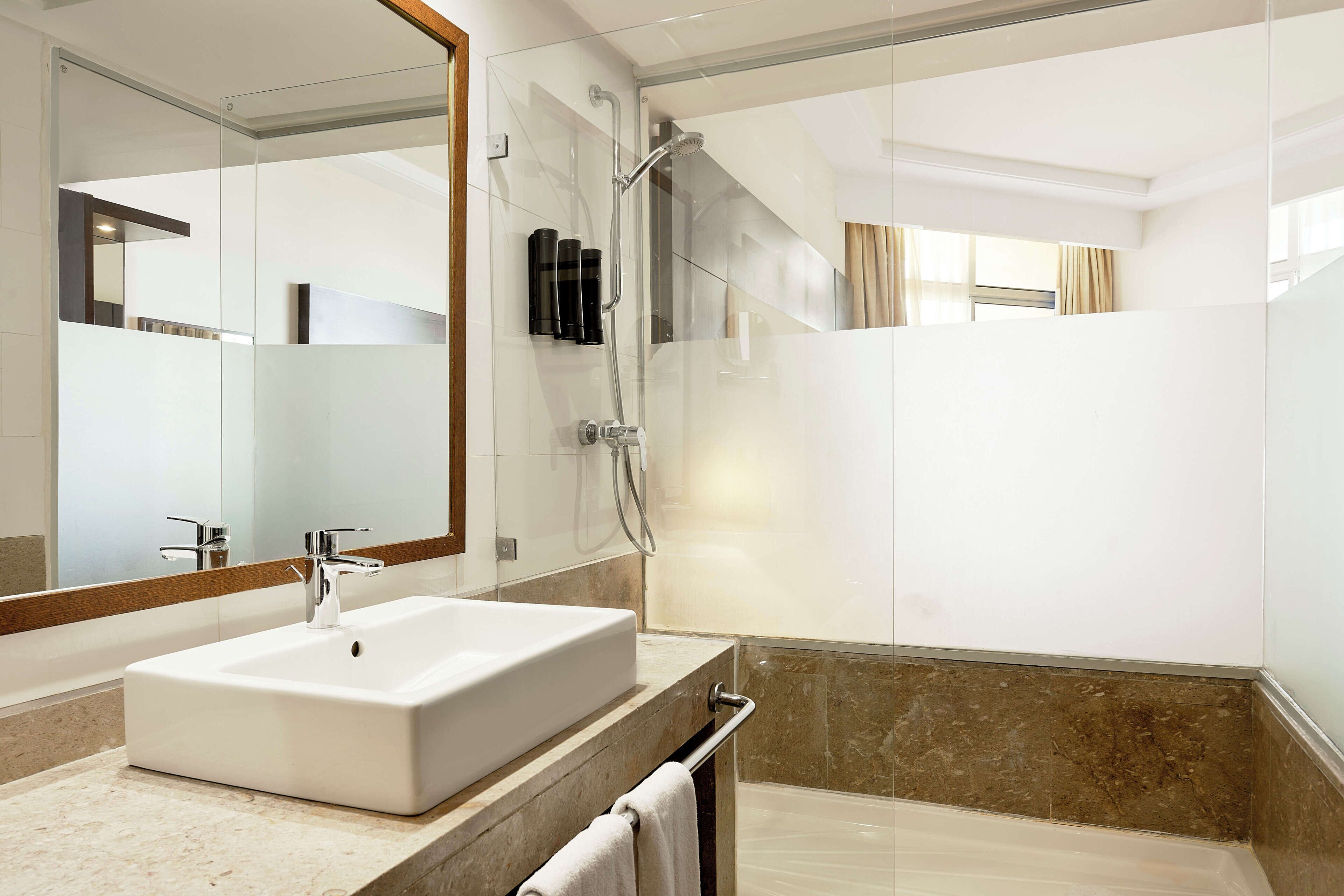 A modern bathroom with a large mirror, a rectangular sink, a shower, and a glass-enclosed shower area.