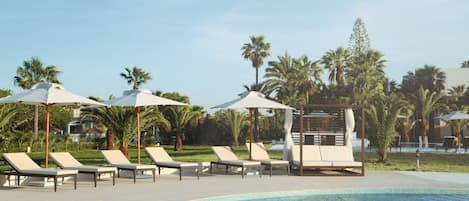 Un espace piscine agrémenté de chaises longues et de parasols, entouré de palmiers.
