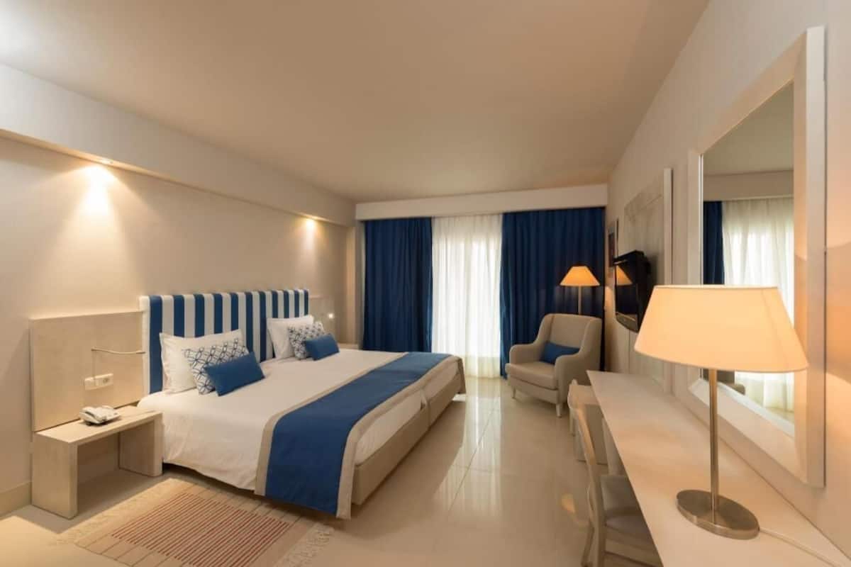 A hotel room with a bed, bedside table, lamp, chair, and a large mirror.