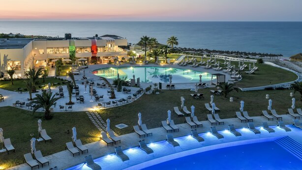 Un complexe hôtelier doté d’une grande piscine, de chaises longues et offrant une vue sur l’océan.
