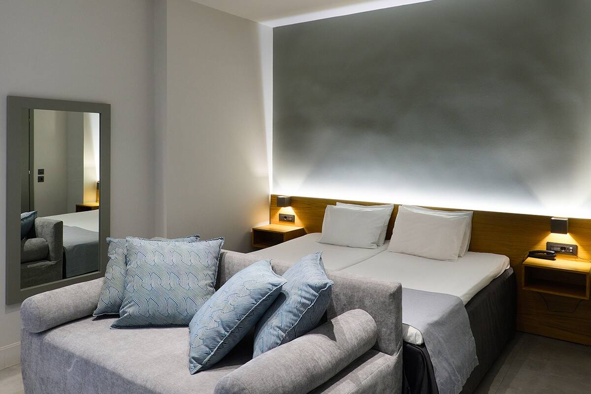 Ein modernes Hotelzimmer mit einem großen Bett, einer Couch, einem Spiegel und Nachttischlampen.