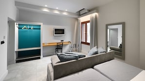 Una habitación de hotel moderna con un sofá gris, un televisor, un escritorio con una silla y un armario con interior verde azulado.