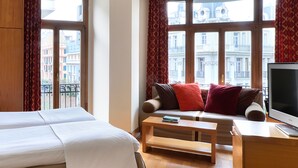 Habitación de hotel con cama, sofá con cojines, una mesita de café y televisión.