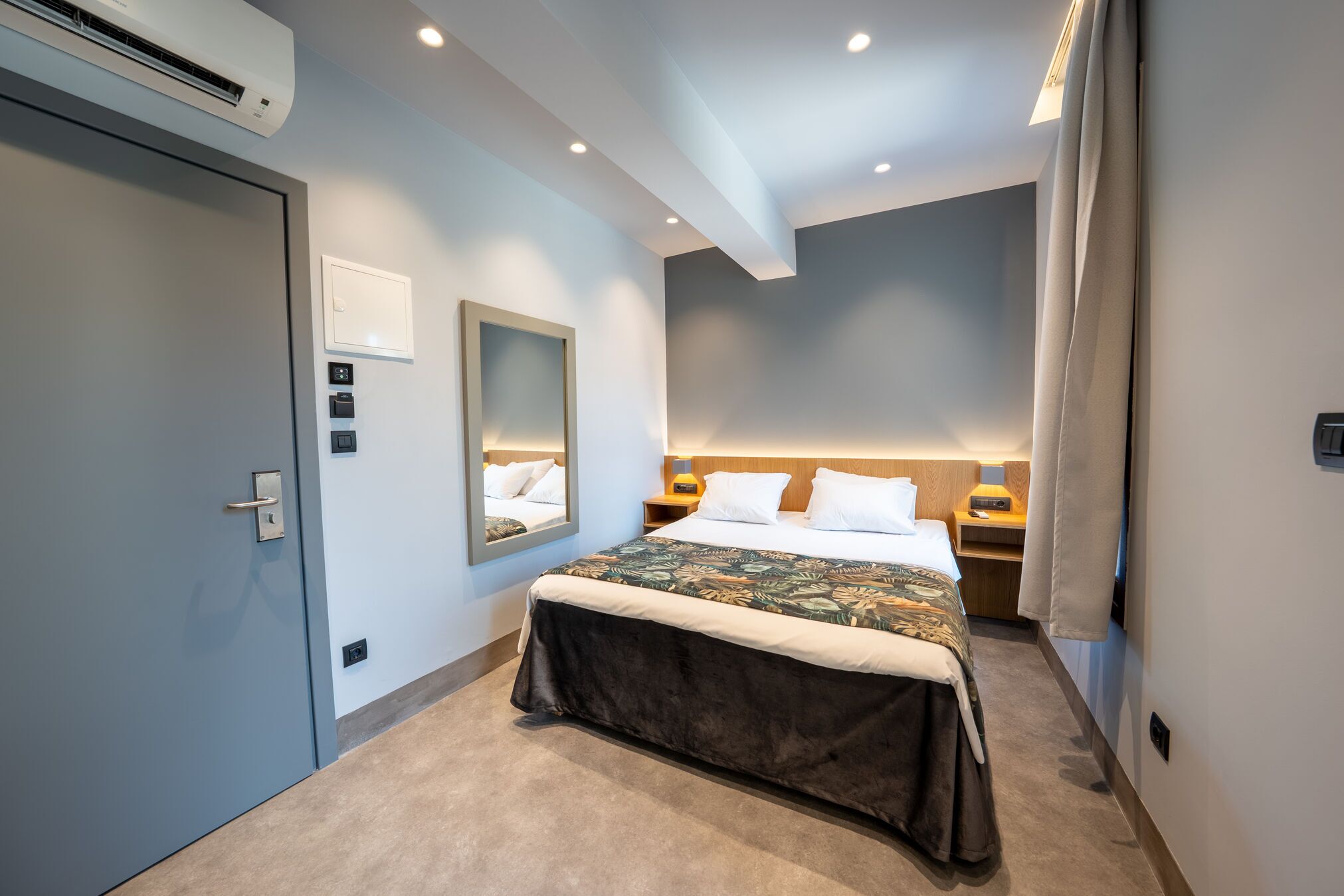 A hotel room with a bed, bedside tables, a mirror, and a door.