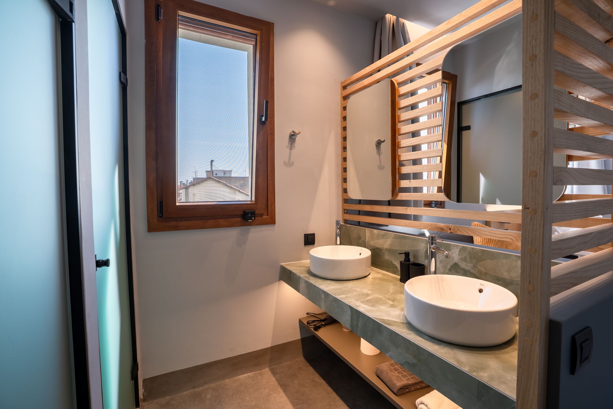 A modern bathroom with two sinks, a large mirror, and a window.