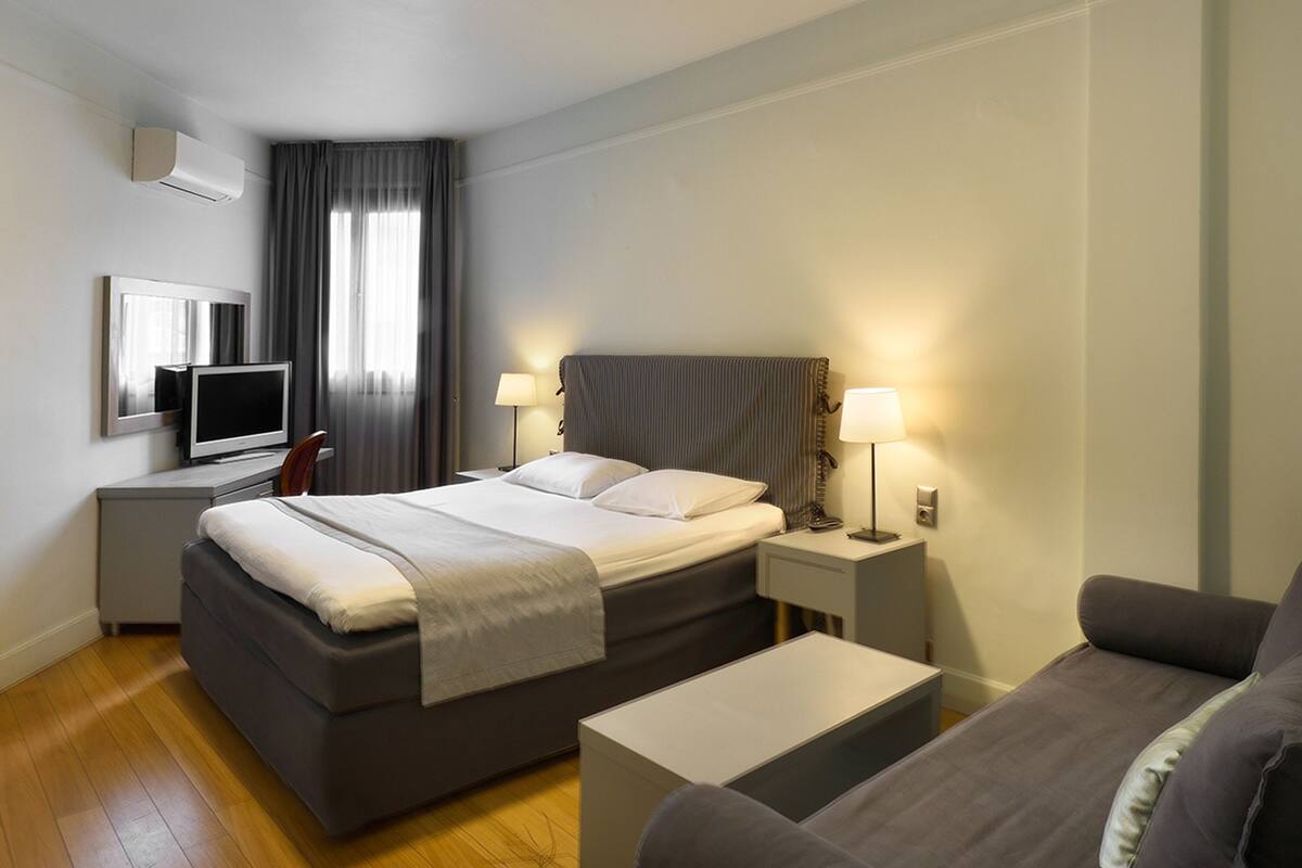 Ein modernes Hotelzimmer mit einem großen Bett, Nachttischen mit Lampen, einem Flachbildfernseher und einem Sofa.