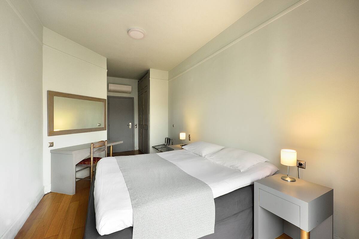 Ein modernes Hotelzimmer mit Bett, Nachttischen, einem Schreibtisch und einem Spiegel.