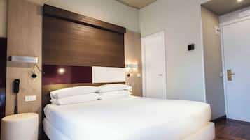 A modern hotel room with a large bed, wooden flooring, and built-in lighting.