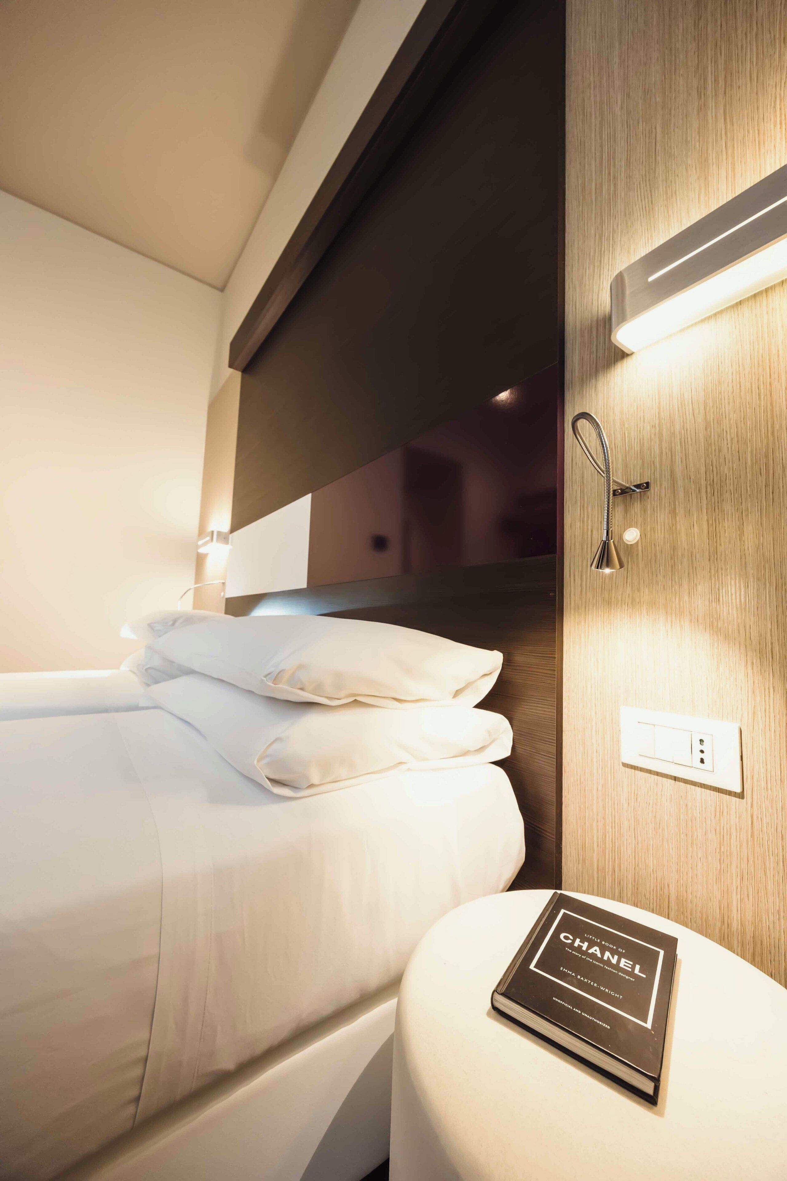 Una habitación de hotel con una cama bien hecha, una mesita de noche con un libro y una lámpara de pared.