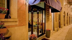 A hotel entrance with a glass door, potted plants, and a dark awning. - Genius Hotel Downtown (Milan)