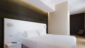 A modern hotel room with a large bed, a white nightstand, and a dark wooden accent wall. - Boston Hotel (Bari)