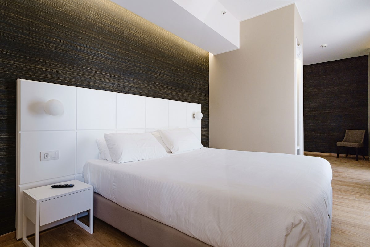 Une chambre d’hôtel moderne avec un grand lit, une table de chevet blanche et un mur d’accent en bois foncé.