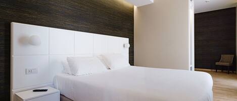 A modern hotel room with a large bed, a white nightstand, and a dark wooden accent wall.