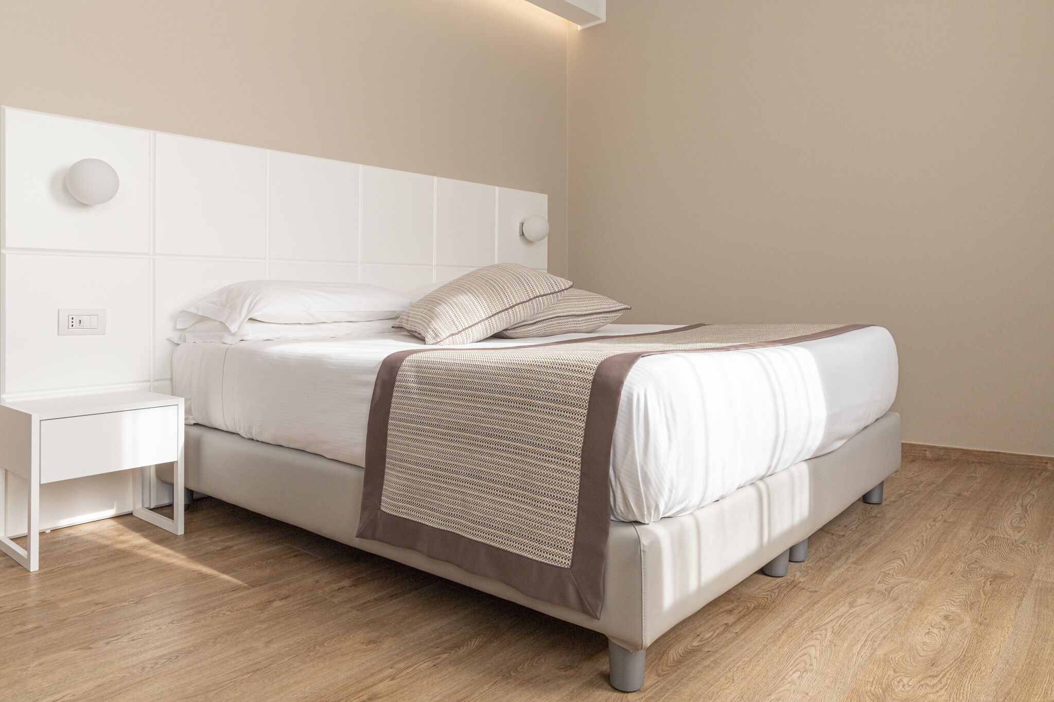 Un dormitorio moderno con cama, mesita de noche blanca y lámpara de pared.