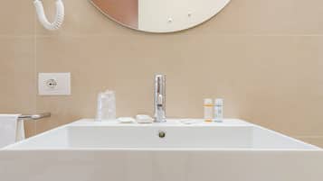 Un baño moderno con un lavamanos grande de color blanco, un espejo redondo y un perchero.