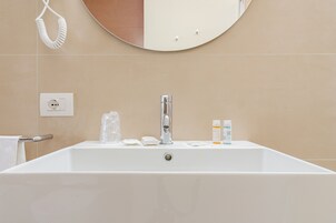 Un baño moderno con un lavamanos grande de color blanco, un espejo redondo y un perchero.