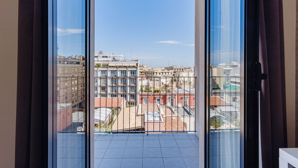 A balcony with a clear view of the cityscape, including buildings and a rooftop garden. - Boston Hotel (Bari)