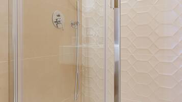 A shower area with a glass door, a showerhead, and a wall-mounted shelf.