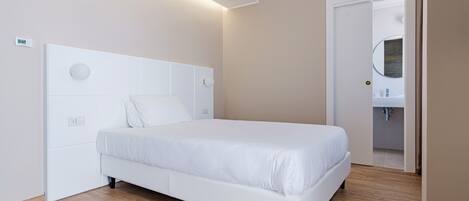 Une chambre moderne avec un lit blanc, une tête de lit ornée de luminaires circulaires et un plancher en bois.