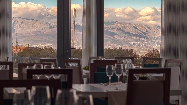 A restaurant with tables set for dining, large windows offering a mountain view. - Príncipe da Beira Hotel (Fundao)