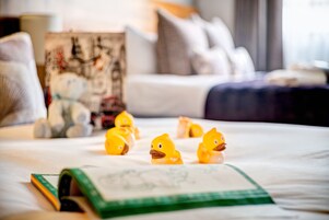 Ein Bett mit einer grün-weißen Bettdecke, ein Buch und mehrere gelbe Gummienten.