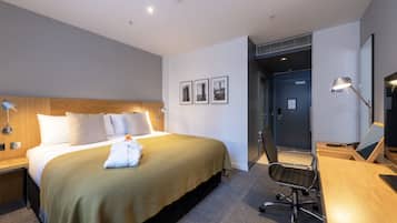 Habitación de hotel con una cama grande, un escritorio, una silla y una puerta que da a otra habitación.