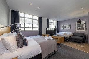 A modern hotel room with a large bed, a desk, a sofa, and a TV.