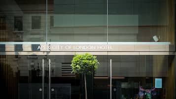 El exterior del Apex City of London Hotel, con fachada de vidrio moderna, una planta en maceta y una escultura decorativa de un toro.