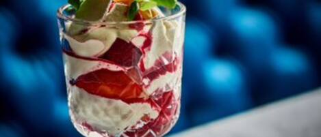 A dessert in a clear glass with layers of cream and fruit, set against a blue background.