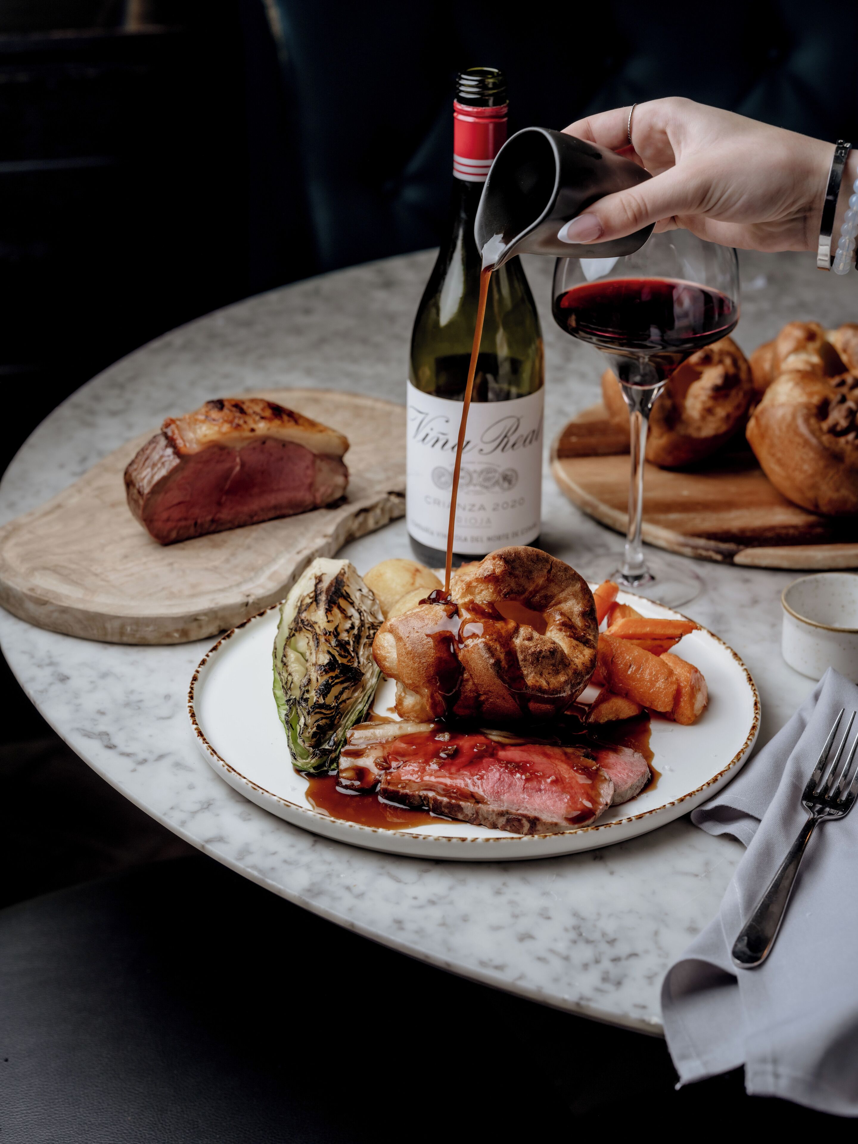 Un plato de comida con una botella de vino y vino tinto siendo servido en una copa.