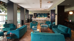 A modern bar area with teal upholstered seating, a bar counter, and a view of the street outside. - Apex City of London Hotel (London)