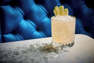 A glass of a light-colored beverage with ice cubes and a garnish on a marble surface.