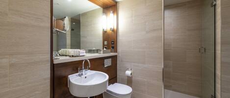 A modern bathroom with a double sink, toilet, and a glass-enclosed shower area.