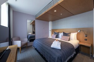 Una habitación de hotel moderna con una cama grande, una mesita de noche, una silla, un escritorio y un espejo.