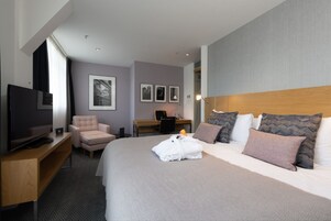 A modern hotel room with a large bed, a desk, a chair, and a television.