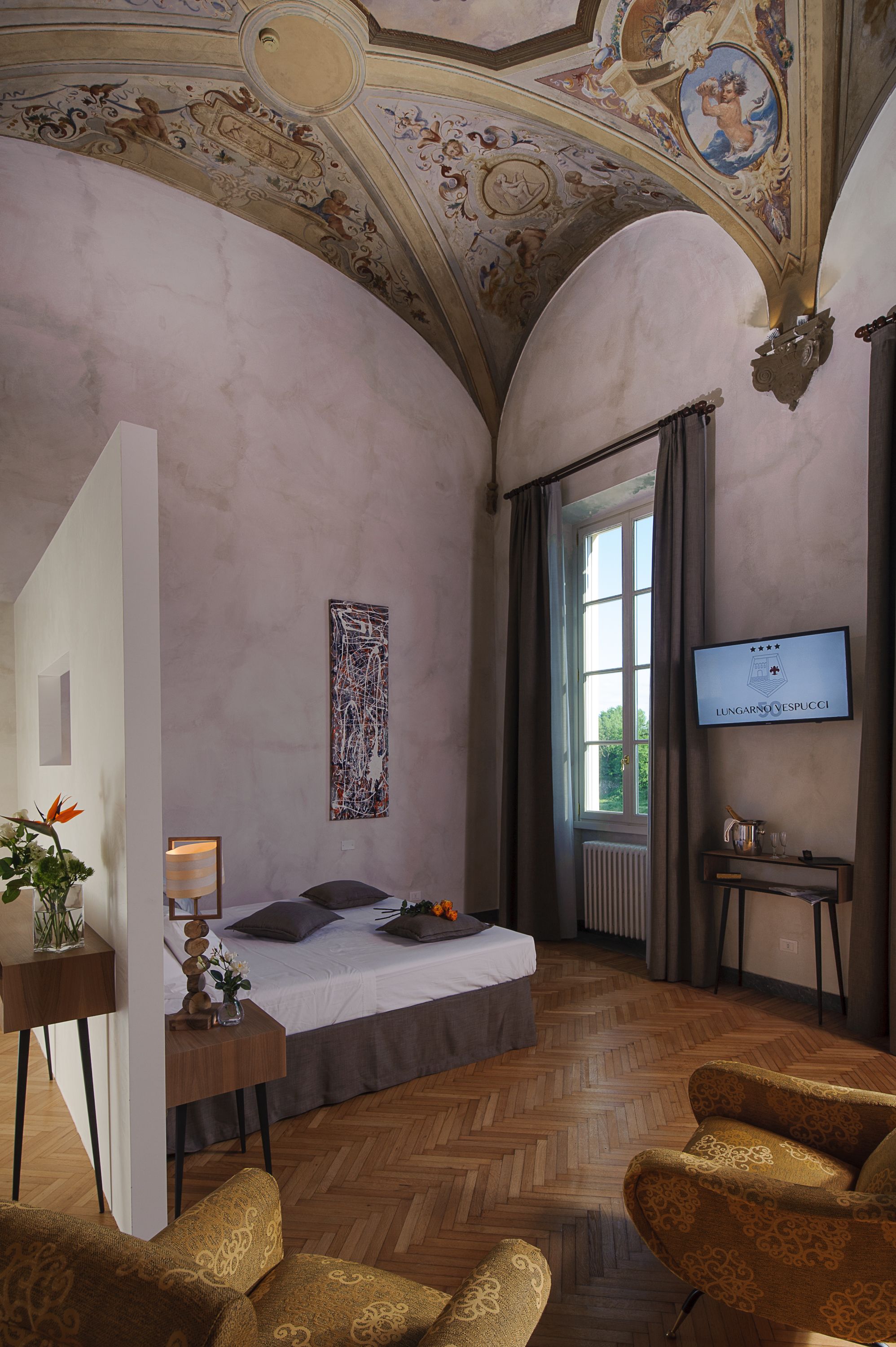 A bedroom with a bed, a desk, a chair, a TV, and a window.