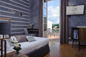 Habitación de hotel con cama, mesita de noche, lámpara y vistas al exterior.