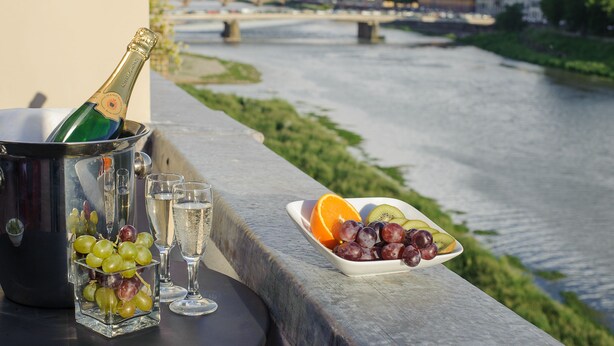 A bottle of champagne in a bucket, glasses, and a plate of fruit by a riverside view.