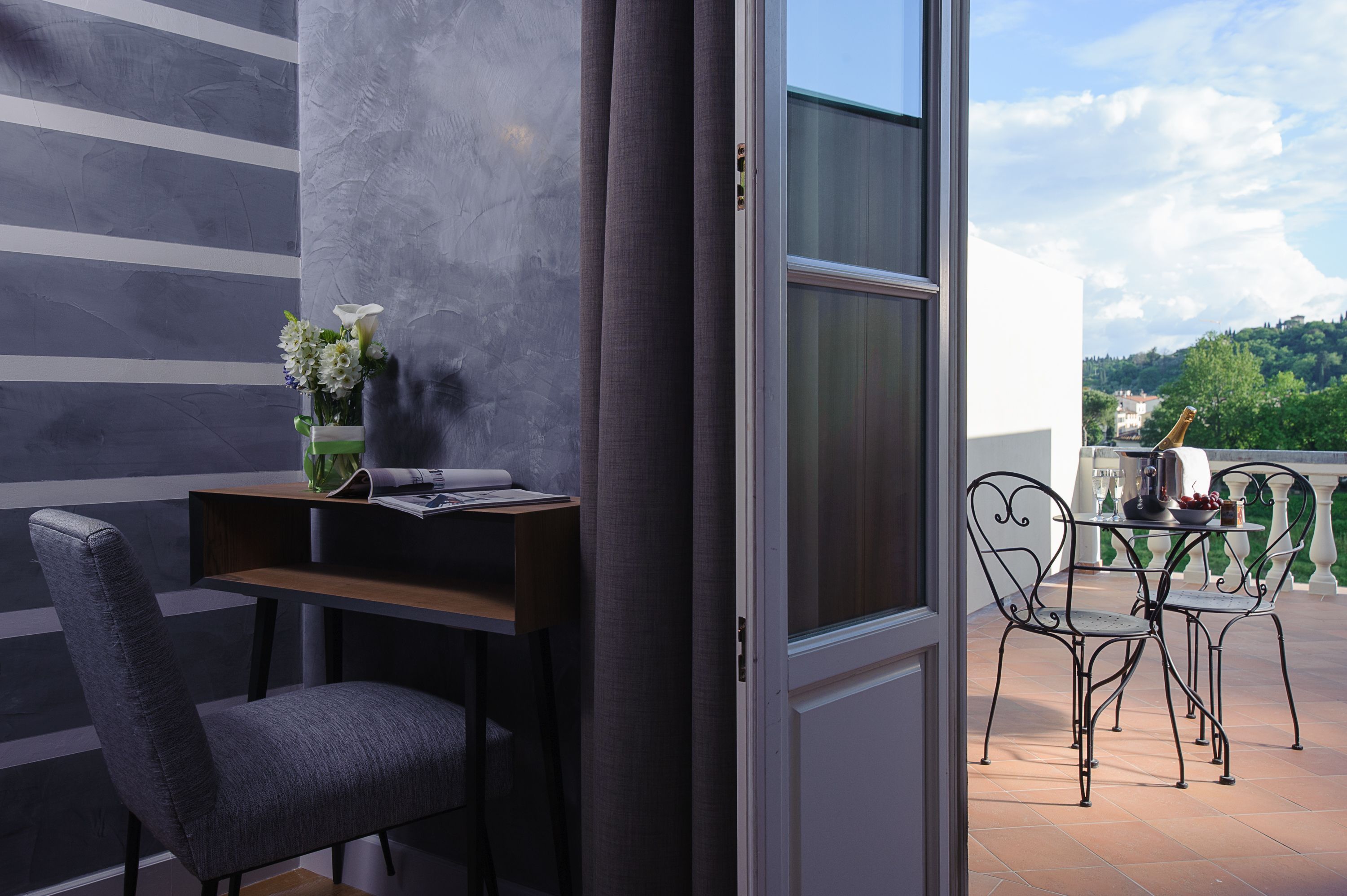 Une chambre moderne avec un mur à rayures grises, un bureau en bois, une chaise grise et un balcon avec une table et des chaises.