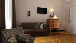 A living room with a sofa, a houndstooth armchair, a wooden cabinet, and a flat-screen TV on the wall.