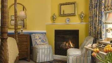 A room with a fireplace, two armchairs, a wooden bed, and a mirror on the wall.