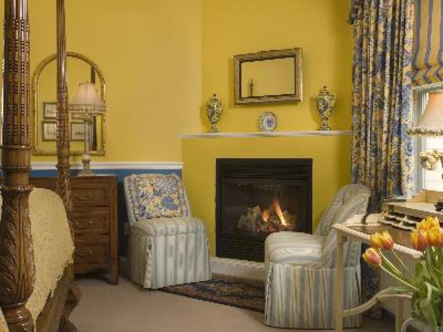 A room with a fireplace, two armchairs, a wooden bed, and a mirror on the wall.