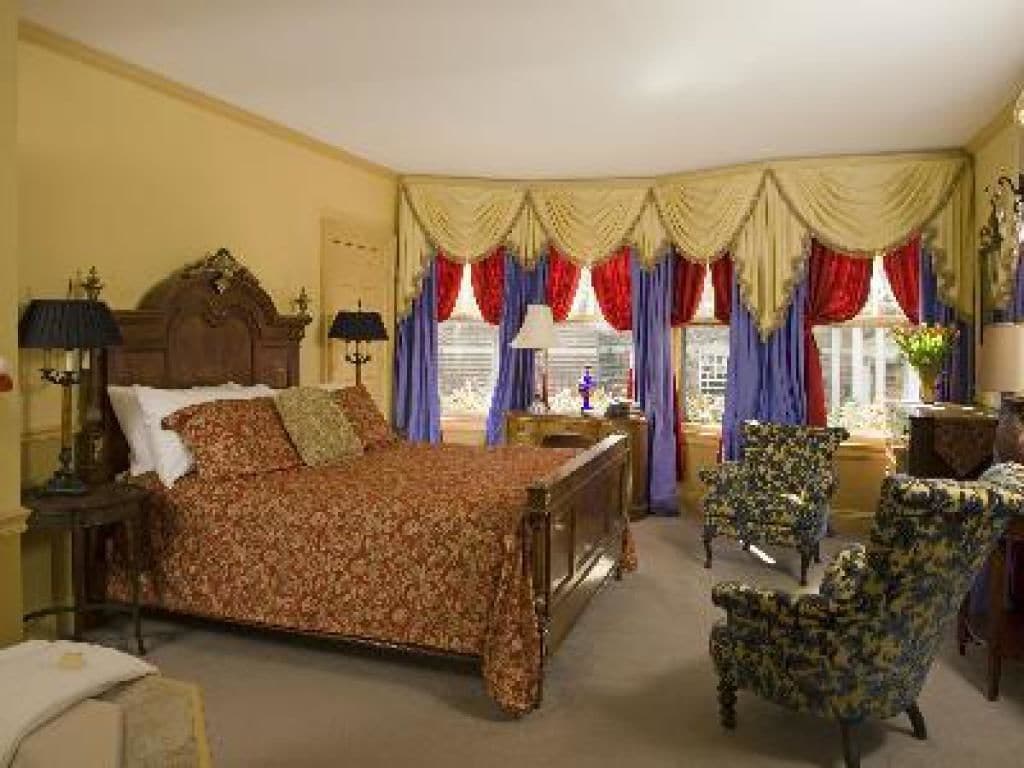 A bedroom with a large bed, two bedside tables, a nightstand, a chair, and a window with curtains.