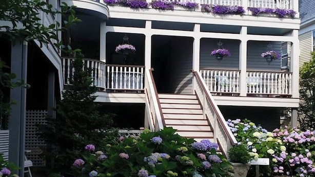 Ein zweistöckiges Gebäude mit weißer Fassade, einer Veranda mit Treppe und Blumenkästen an den Balkonen.