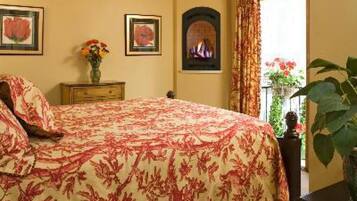 A bedroom with a floral bedspread, a fireplace, and a large window with curtains.